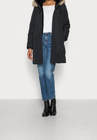 Sort skumpolstret parka med en pelsekantet hætte, lynlåslukning, to sidelommer, parret med blå cropped jeans og sorte ankelstøvler.