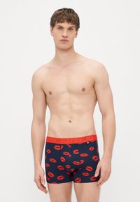 Námornícke boxerky s červeným potlačeným motívom pier, vybavené elastickým pásom s nápisom „HAPPY“ v tučnom písme. Vyrobené z pružnej látky pre pohodlie.