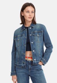 Denim jacket in medium blue with a collared neckline, button closure, and two chest pockets; features stitching accents and a relaxed fit.