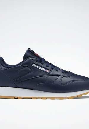 Navy blue leather sneaker with a white and gum sole, featuring lace closure, Reebok branding, and streamlined design.