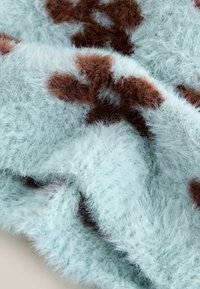 Tela de pelaje sintético en azul claro con manchas marrones, que presenta una textura suave y esponjosa. El material es grueso y mullido.