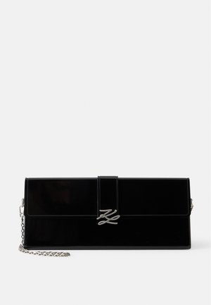 Pochette rectangulaire noire brillante avec bretelle chaîne argentée et fermoir aux initiales argentées entrelacées sur le rabat avant.