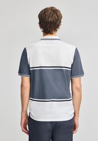 Pikétröja i vitt och grått, med korta ärmar, krage och horisontella ränder. Materialet ser slätt ut med en strukturerad yta.