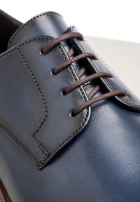 Zapato de vestir de cuero azul marino con una textura suave, cordones marrones y costuras visibles a lo largo de los bordes y ojales.
