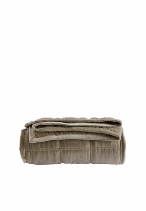 Couverture marron douce et matelassée, soigneusement pliée avec des lignes de couture visibles sur fond blanc.