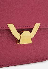Borsa a mano in pelle fucsia con chiusura in metallo dorato caratterizzata da un design distintivo a forma di ala e cuciture a contrasto lungo i bordi.