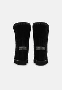 Botas de tobillo de ante negro con forma redondeada, que cuentan con costuras decorativas y un parche metálico de marca en la parte trasera. Suelas de goma planas.