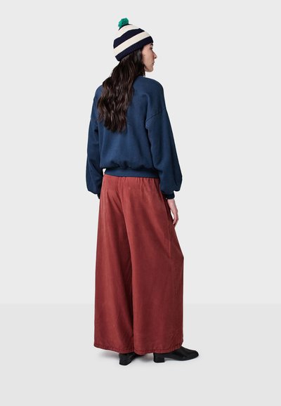 Marinblå oversized sweatshirt med ribbad nederkant, tillsammans med rostfärgade vida corduroybyxor. Modellen bär en randig stickad beanie med pom-pom.