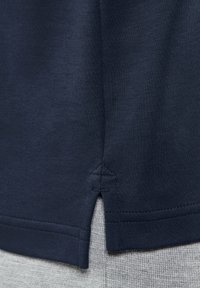 Navyblaue Baumwollbluse mit seitlichen Schlitzen am Saum, die eine glatte Textur und präzise Nähdetails aufweist.