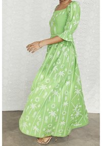 Lång, grön maxikjol med fyrkantig halsringning och trekvarts ärmar med klockformat avslut. Har vita palm- och solmönster över hela plagget. Texturerad tyg.