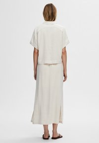 Light beige linen two-piece outfit featuring a short-sleeved top and a long skirt with side slits, simple design, and relaxed fit.