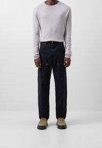 Jasnoszara koszula z długim rękawem, luźne ciemnoniebieskie spodnie z przednimi kieszeniami oraz szaro-zielone buty z żółtymi akcentami. Prosty design i faktura.