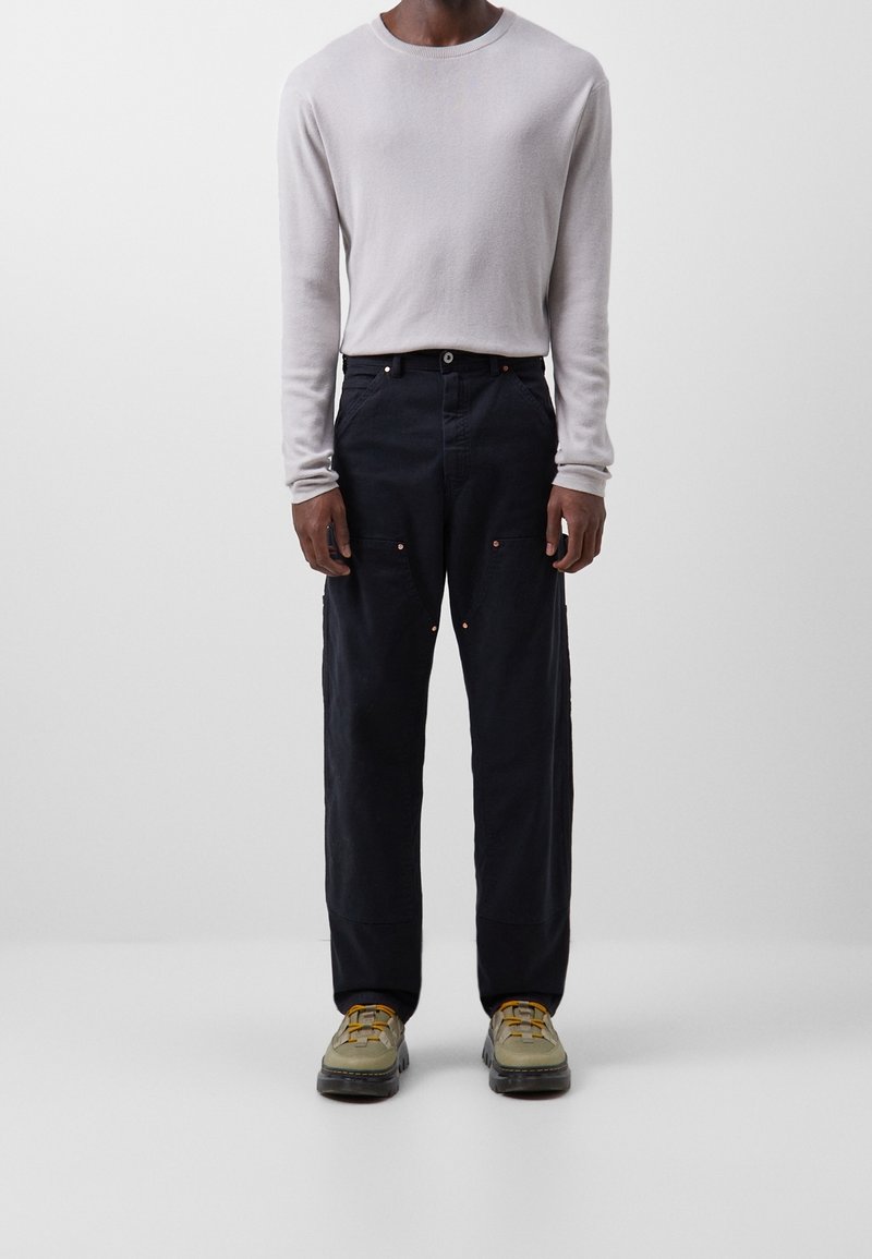 Jasnoszara koszula z długim rękawem, luźne ciemnoniebieskie spodnie z przednimi kieszeniami oraz szaro-zielone buty z żółtymi akcentami. Prosty design i faktura.