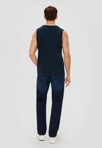 Navy sleeveless shirt paired with dark denim jeans. The jeans feature back pockets and are styled with white sneakers.
