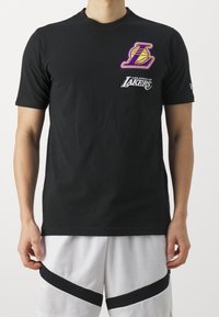 Svart kortärmad t-shirt i bomull, med en lila och guld Los Angeles Lakers-logotyp och vit text på framsidan.