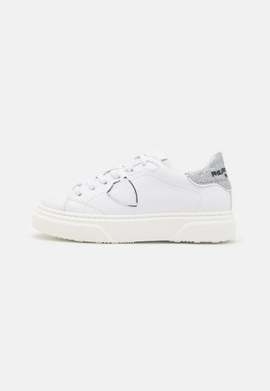 Baskets en cuir blanc avec un bout rond, présentant un accent de talon argenté pailleté et une semelle en caoutchouc texturée. Les lacets sont blancs.