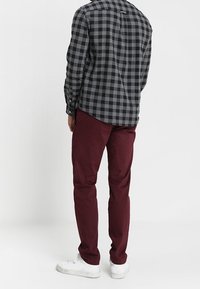 Gecheckeerd zwart en grijs overhemd met een ronde zoom, gecombineerd met kastanjebruine broek en witte sneakers. Het overhemd heeft knoopmanchetten.
