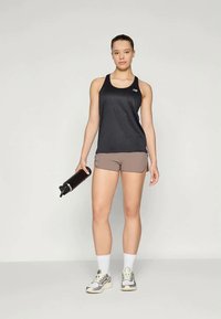 Μαύρο αθλητικό αμάνικο μπλουζάκι, ανοιχτό καφέ σορτσάκι, κρατώντας ένα μαύρο μπουκάλι νερού. Συνδυασμένο με άσπρες κάλτσες και γκρι αθλητικά παπούτσια, με υφή σόλας.