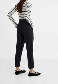 Pantalon noir longueur cheville à taille haute, associé à un haut blanc ajusté avec des rayures noires horizontales. Texture douce, sans motifs visibles.