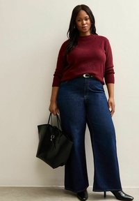 Maglione a maglia bordeaux, jeans a vita alta blu scuro a gamba larga, décolleté nere con tacco a spillo e una grande borsa nera con manici doppi.