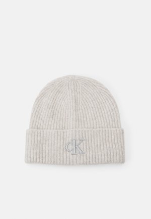 Gorro de punto acanalado de color beige claro con un dobladillo, bordado con un pequeño logo "cK" en gris en el centro frontal.