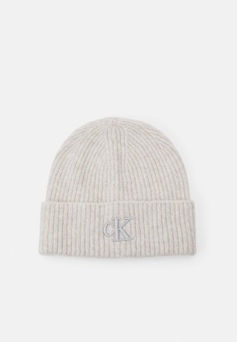 Gorro de punto acanalado de color beige claro con un dobladillo, bordado con un pequeño logo "cK" en gris en el centro frontal.