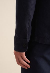 Camicia blu navy con tessuto testurizzato, polsini con dettaglio di bottone e design slim fit visibile sul polso e sulla mano.