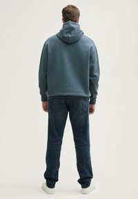 Niebieska bluza z kapturem, o gładkiej fakturze; zestawiona z ciemnoniebieskimi dżinsami i białymi trampkami, pokazana z tyłu.