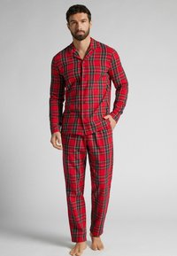 Červené kostkované pyžamo vyrobené z měkké tkaniny, obsahující košili na knoflíky s dlouhými rukávy a odpovídající kalhoty, prezentující klasický kostkovaný vzor.
