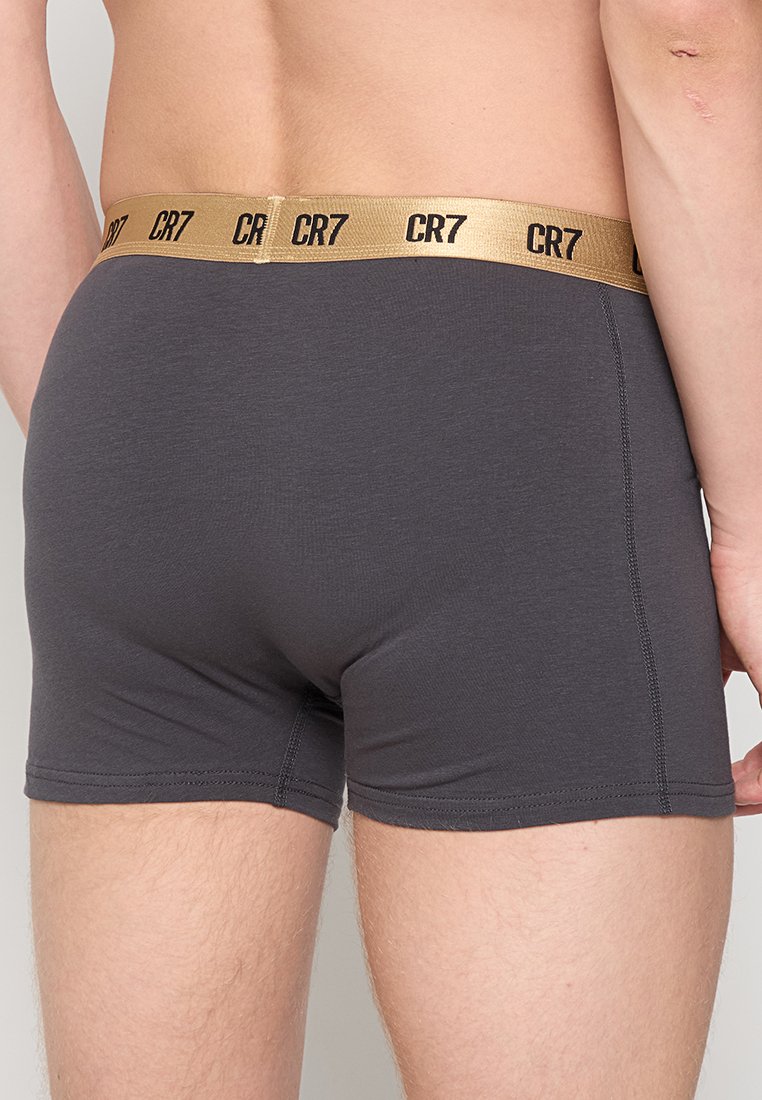 Graue Boxer Shorts mit einer glatten Textur, ausgestattet mit einem goldenen elastischen Bund, der mit "CR7" beschriftet ist. Enganliegend mit kurzer Beinbedeckung und flachen Nähten.