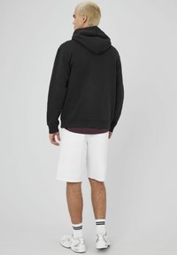 Un sweat à capuche noir avec une coupe décontractée, associé à un short en denim blanc. Des baskets blanches avec des accents argentés et des chaussettes rayées.