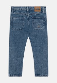 Pantalones vaqueros de mezclilla azul medio con corte de pierna recta, que presentan dos bolsillos traseros, un parche de cuero con el logo y detalles de costura sutiles.