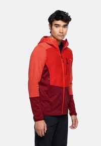 Herren-Zip-Jacke in Rot und Bordeaux, ausgestattet mit einer Kapuze, strukturiertem Stoff, zwei Reißverschlusstaschen und einem farblich abgesetzten Design.