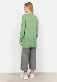 Grön stickad cardigan med en lång, lös passform och ribbade detaljer. Åtföljs av grå vida byxor och vita sneakers.
