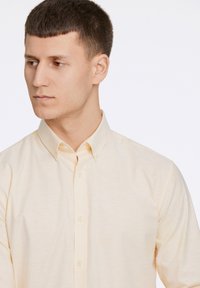 Camicia button-up gialla chiara con una texture morbida, colletto classico e dettagli di cucitura visibili. Presenta una vestibilità slim.