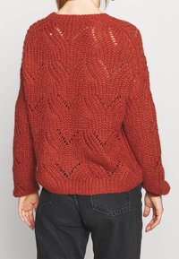 Gestrickter Pullover in tiefrot mit einem strukturierten, offenen Muster. Mit Rundhalsausschnitt und langen Ärmeln. Lockere Passform mit geripptem Saum.