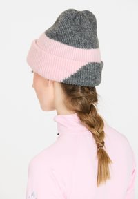 Neulepipo, jossa on vuorottelevat harmaan ja vaaleanpunaisen raitoja, pehmeällä tekstuurilla ja tiiviillä istuvuudella. Käännetty reunatyyli, jossa on kapeneva yläosa.