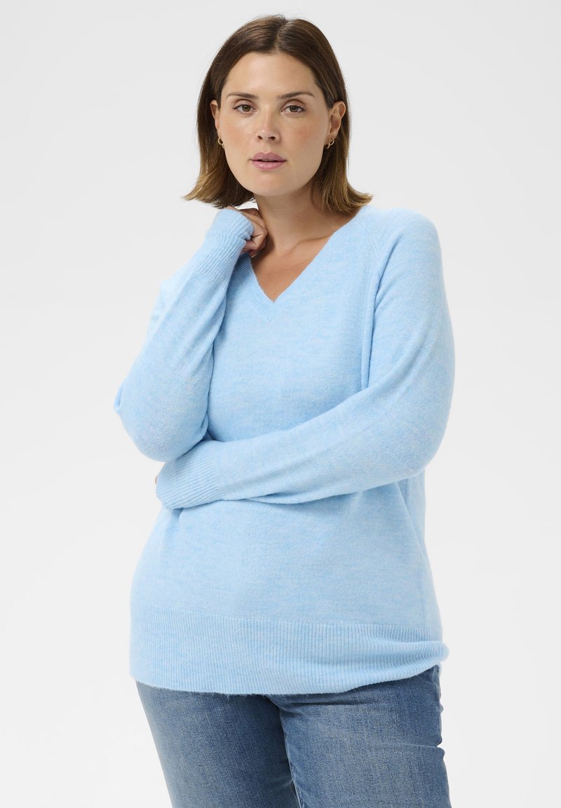 Helles blaues V-Ausschnitt-Sweatshirt aus einem weichen, strukturierten Stoff mit langen Ärmeln und gerippten Bündchen, kombiniert mit blauen Jeans.