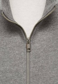 Suéter de forro polar gris con cremallera metálica, que presenta un cuello alto y un forro interior suave. Tela texturizada con un patrón jaspeado.