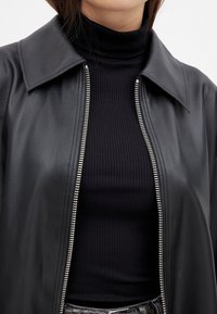 Melnas ādas jaka ar plašu apkakli, metāla rāvējslēdzēja detaļa, apvienota ar ribotu melnu augsto apkakli. Gluda tekstūra, pielāgota piegriezuma forma.