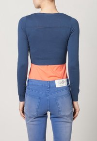 Marinblå kortärmad tröja med långa ärmar, ribbad nederkant, kombinerad med en korallfärgad topp under. Ljust blå jeans med bakfickor och label.