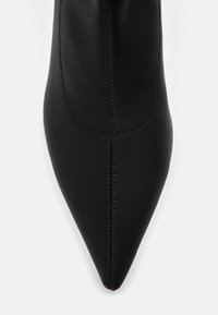 Crne čizmice s oštrom točkom izrađene od glatkog materijala. Sadrže vidljivo šivanje duž bočnih strana i elegantan, sužen dizajn.