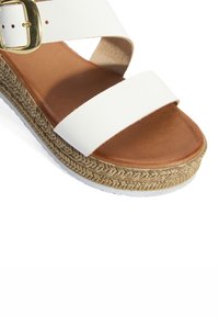Sandale espadrille blanche avec de larges brides et une boucle dorée, dotée d'une semelle intérieure en cuir marron et d'une semelle en jute tressé texturée.