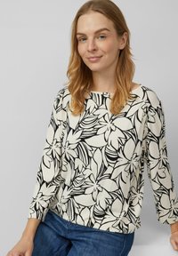 Langärmliges Oberteil mit Blumenmuster, das einen cremefarbenen Hintergrund mit schwarz gezeichneten Blumen und Blättern zeigt, ergänzt durch eine lockere Passform.