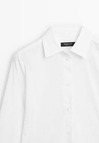 Bílá halenka s dlouhým rukávem a klasickým límečkem, s knoflíkovým zapínáním a hladkým textilním povrchem. Štítek nese nápis "Massimo Dutti." Čistý, minimalistický design.