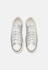 Stříbrné plátěné tenisky s bílými gumovými špičkami, černými detaily a béžovými tkaničkami. Texturovaný povrch s logem "Converse All Star" na jazyku.