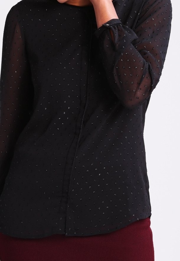 Blusa nera trasparente con piccoli accenti di punti argentati, maniche lunghe e chiusura davanti con bottoni. Tessuto morbido con orlo leggermente curvato.