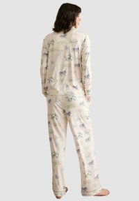 Conjunto de pijama crema con un estampado de animales juguetón en colores pastel. El material parece suave, con mangas largas y pantalones de corte holgado.