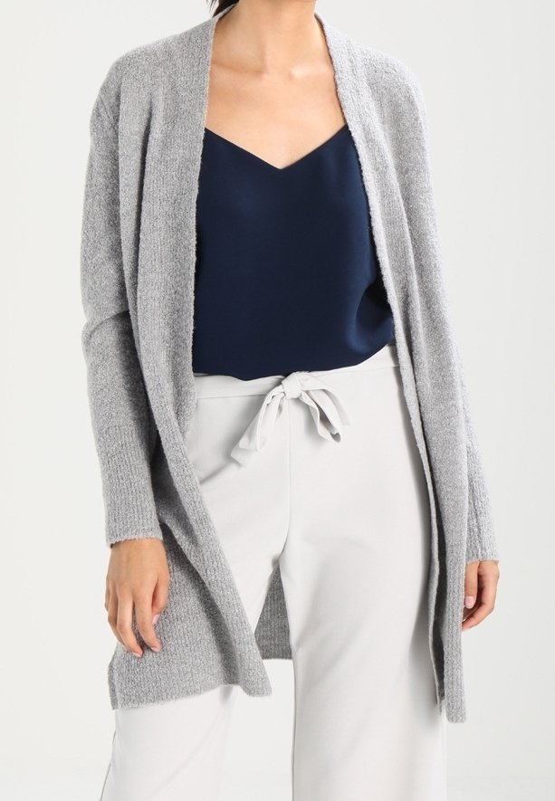 Grå stickad cardigan med öppet front, långa ärmar och ribbad textur, bärs över en marinblå linne och vita byxor med dragsko.