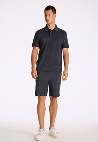 Meripaita ja siihen sopivat shortsit, jotka on valmistettu teksturoidusta kankaasta. Ominaisuuksiin kuuluu kaulus, lyhyet hihat ja valkoiset tennarit.